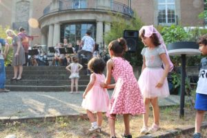 Kinder in Festtagskleidern hören der Bigband zu